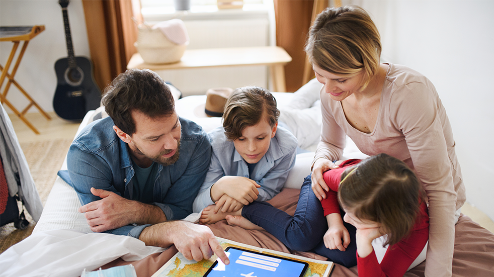 A family of four using a tablet and atlases to plan a holiday together